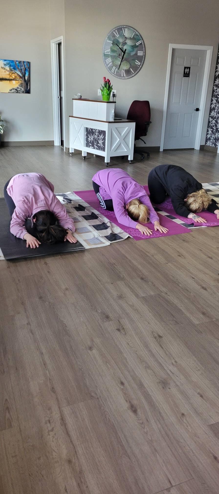 Three women practicing yoga together on mats in Kacie Auffert's yoga class at Wrobel Massage Therapy.